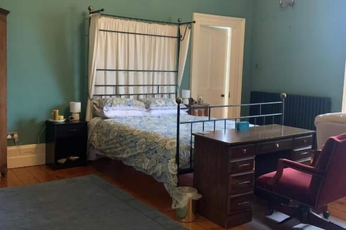 A bedroom with a bed, a desk, a chair, a radiator, and a window.
