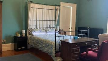 Un dormitorio con cama, escritorio, silla, radiador y ventana.