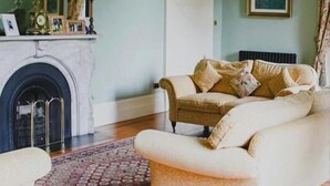 A living room with a fireplace, a sofa, a chair, and a patterned rug. - Ballynacree Manor House  (Ballymoney)
