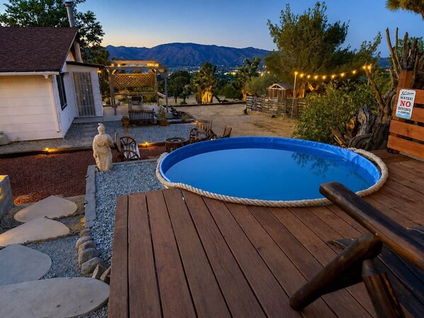 Una terraza de madera con piscina, escalones de piedra y una estatua.