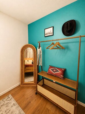 A room with a teal wall, a wooden floor, a rattan bench, a mirror, a hat, and a framed picture. - Coyote Ranch | Western Desert Escape (Yucca Valley)