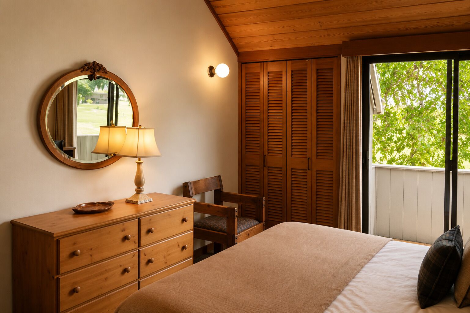Un dormitorio con cama, cómoda, silla, espejo y ventana con vistas a follaje.