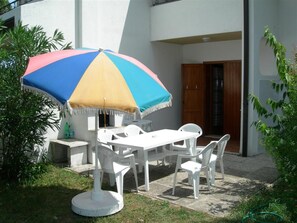 An outdoor patio with a white table and chairs, a colorful umbrella, and a door in the background. - Charming two Level Villa With Garden and BBQ (San Michele al Tagliamento)