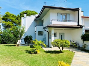 A two-story building with a balcony, a bicycle parked outside, and a well-maintained lawn. - Charming two Level Villa With Garden and BBQ (San Michele al Tagliamento)