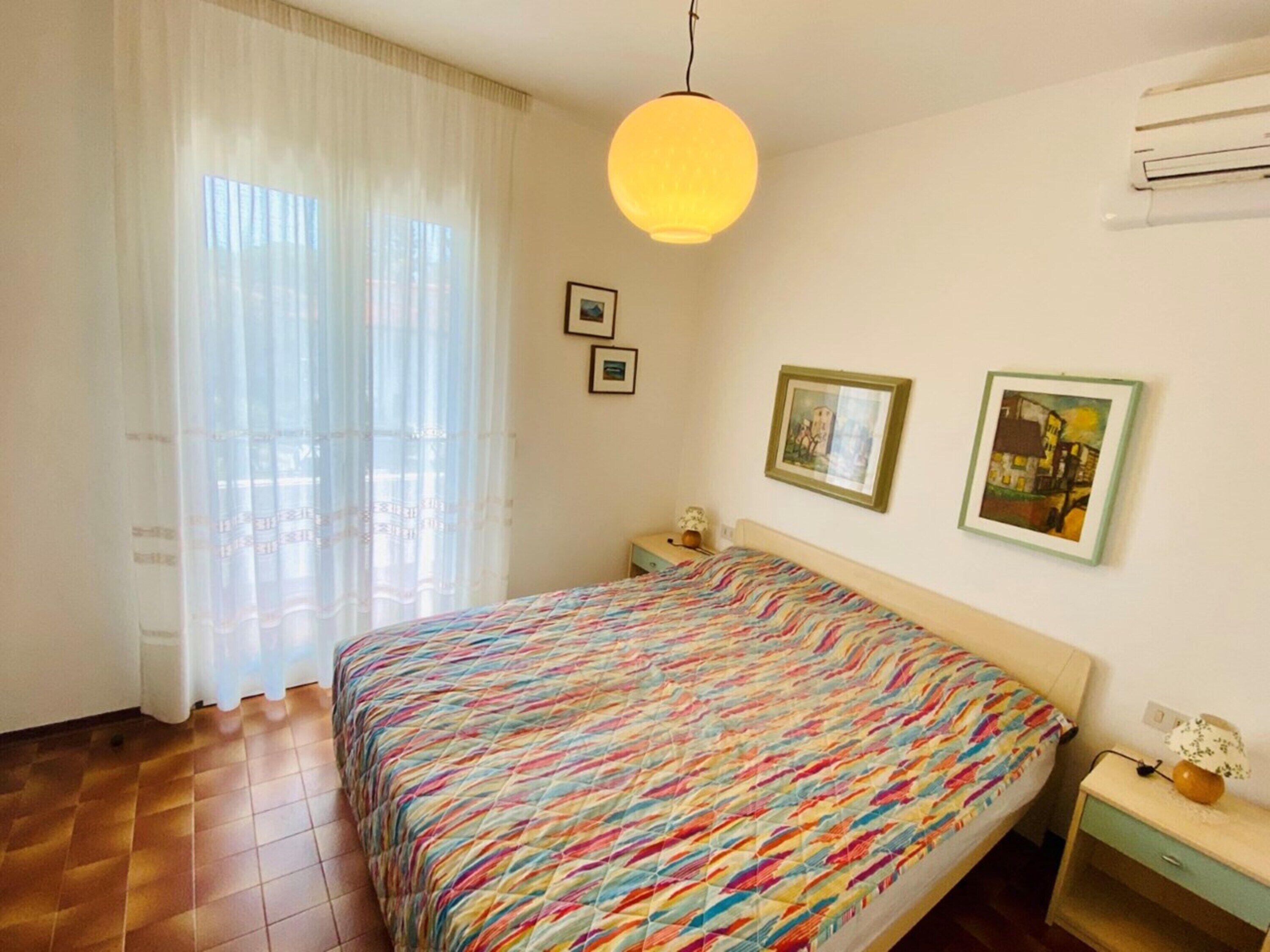 A bedroom with a bed, a nightstand, a lamp, and a window with curtains.