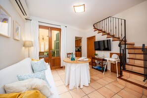 A living room with a sofa, a dining table, a TV, and a staircase. - Holiday Home 'Es Port' with Wi-Fi (Porto Cristo)