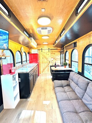 A train car interior with a kitchen area, seating, and large windows.