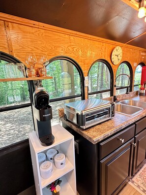 A kitchen with a Keurig coffee maker, a toaster oven, and a sink. There are three windows with arched tops, and a clock on the wall.