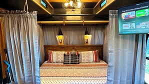 Un dormitorio acogedor con cama, cortinas, un sofá y un televisor mostrando una lista de canales.