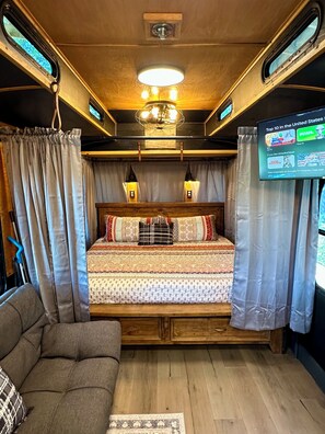 A cozy bedroom with a bed, curtains, a couch, and a TV displaying a list of channels.