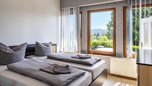 Un dormitorio con dos camas, un ventanal con vistas a la vegetación y un radiador.