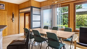 Una habitación con paneles de madera, una mesa grande y sillas, una chimenea y ventanas amplias.