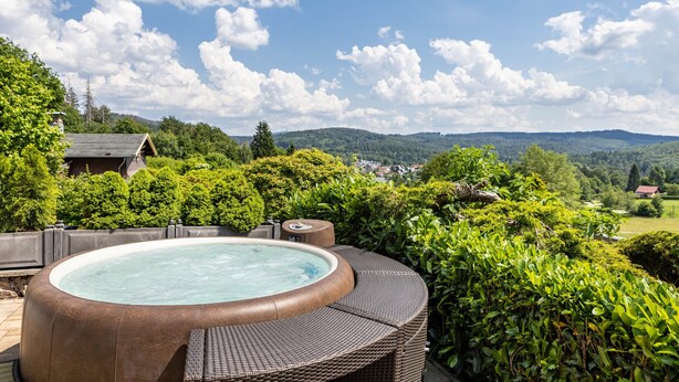 Un jacuzzi con asientos de mimbre, rodeado de abundante vegetación y vistas a colinas distantes.
