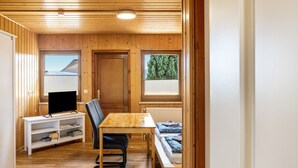 A wooden-paneled room with a television on a white stand, a wooden table, a bench, and a window with a view of trees. - Studio Apartment with Mountain View, Private Terrace and Wi-Fi (Ruhla)