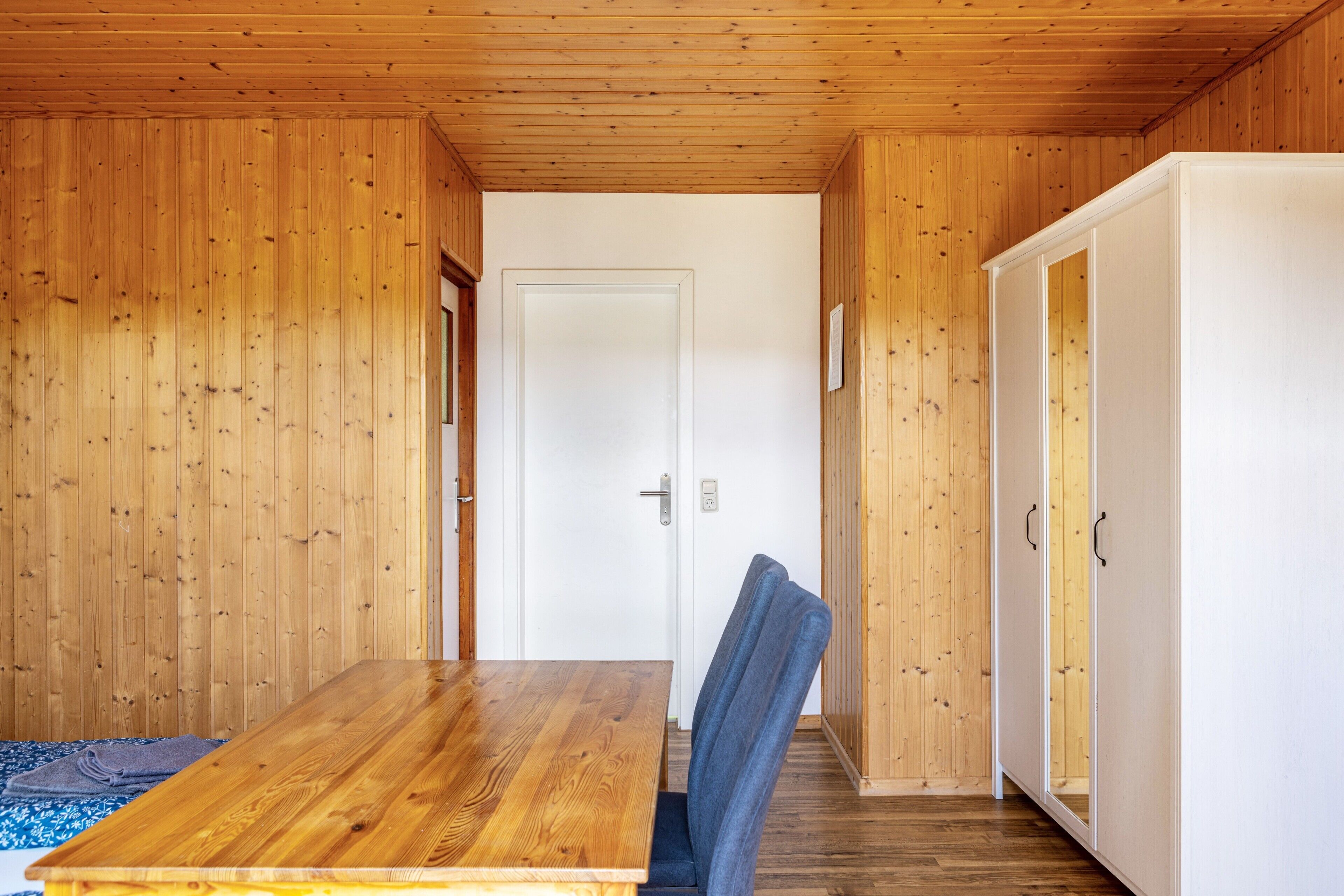 Une pièce aux murs lambrissés, avec une table en bois et une chaise bleue.