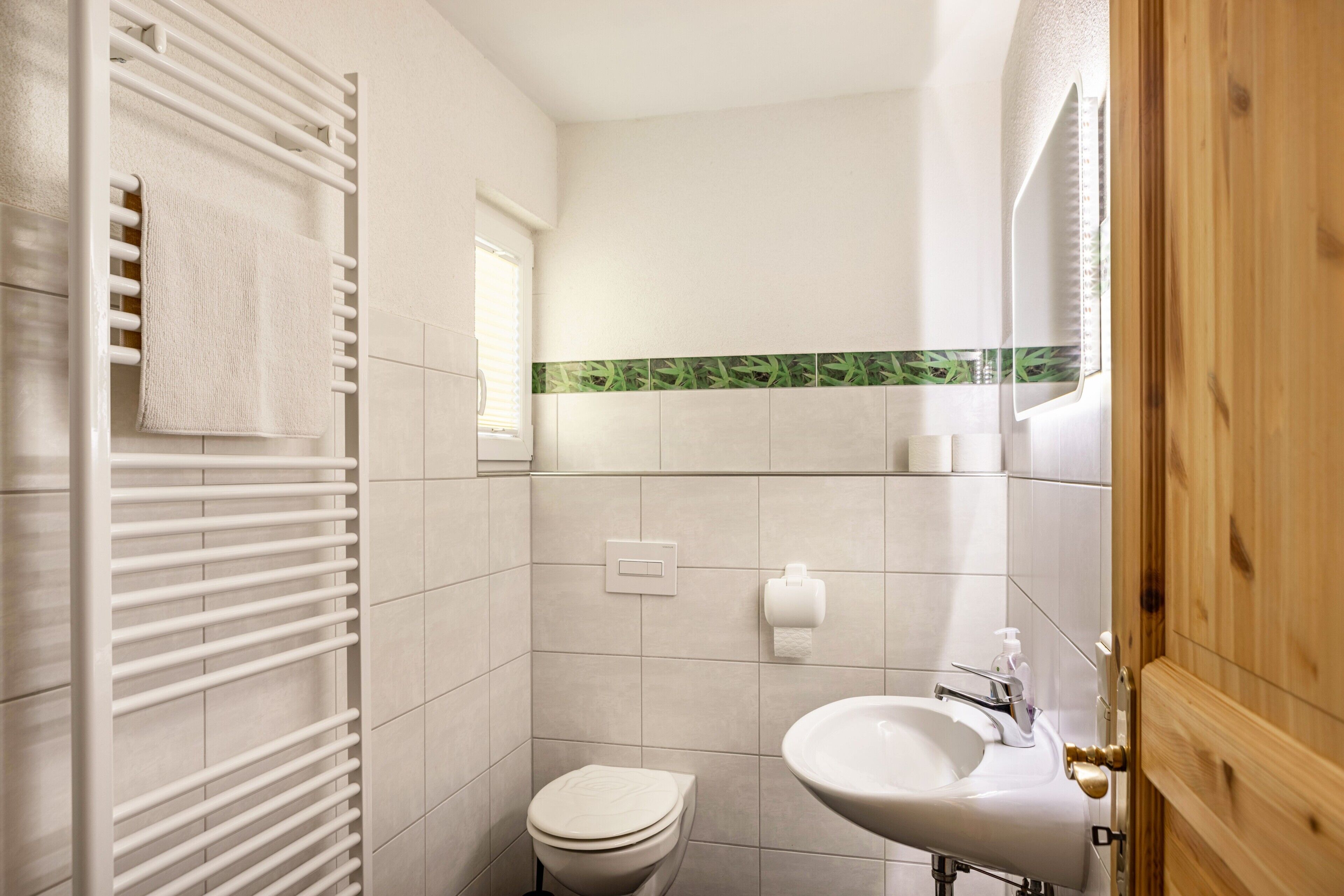 A bathroom with a white toilet, a sink, a towel rack, and a window.
