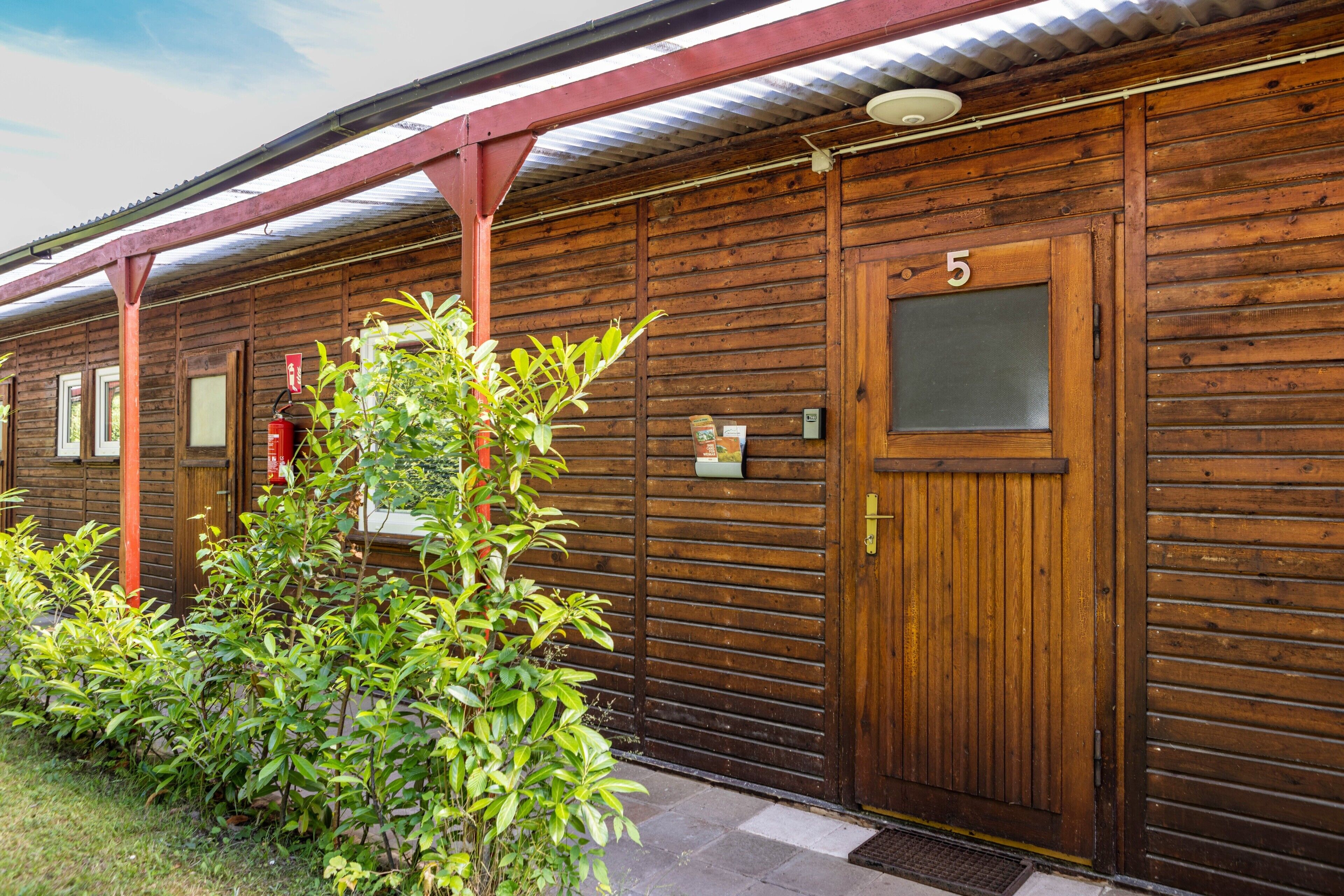 Un bâtiment en bois avec le chiffre « 5 » sur la porte, une petite fenêtre et un auvent en métal.
