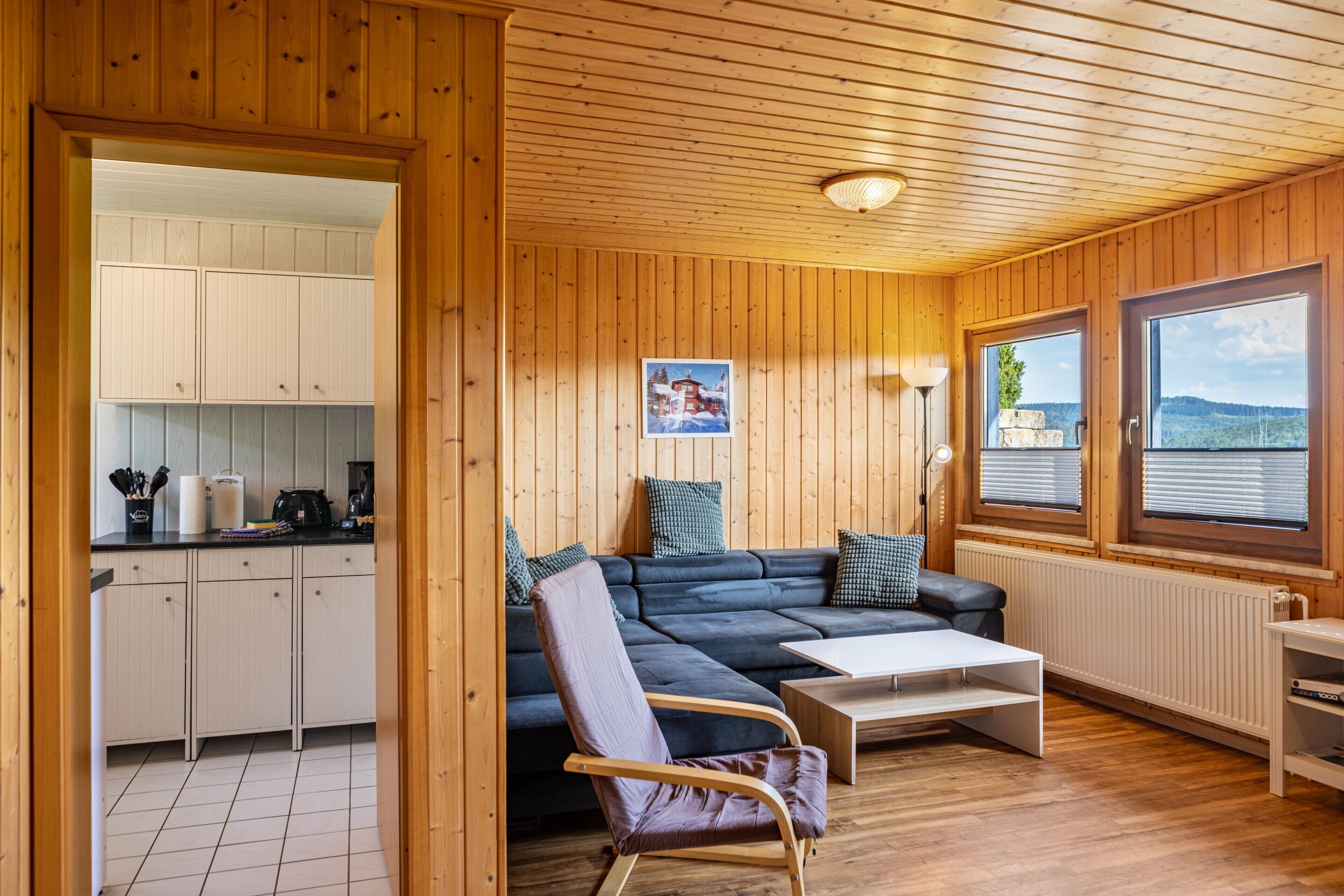 Et træinteriør med en sofa, en lænestol, et bord og et tekøkken.