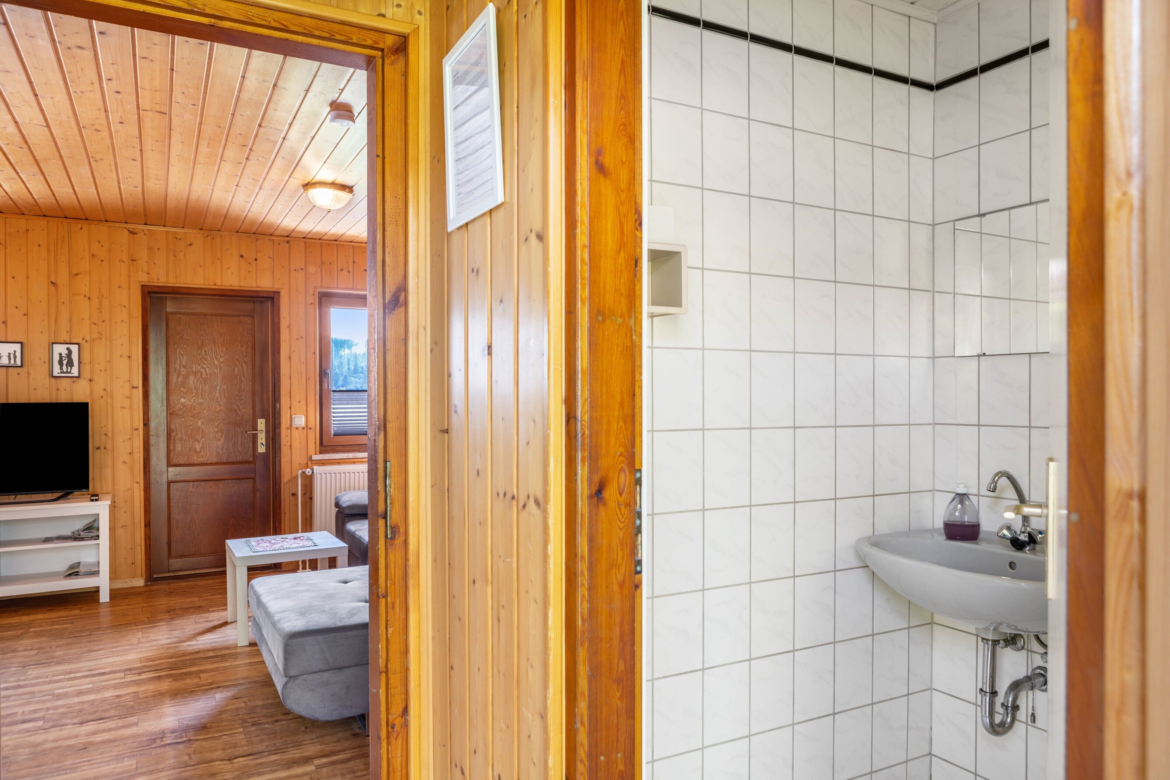 Ein Holzinterieur mit Fernseher, Sofa und gefliestem Badezimmer.