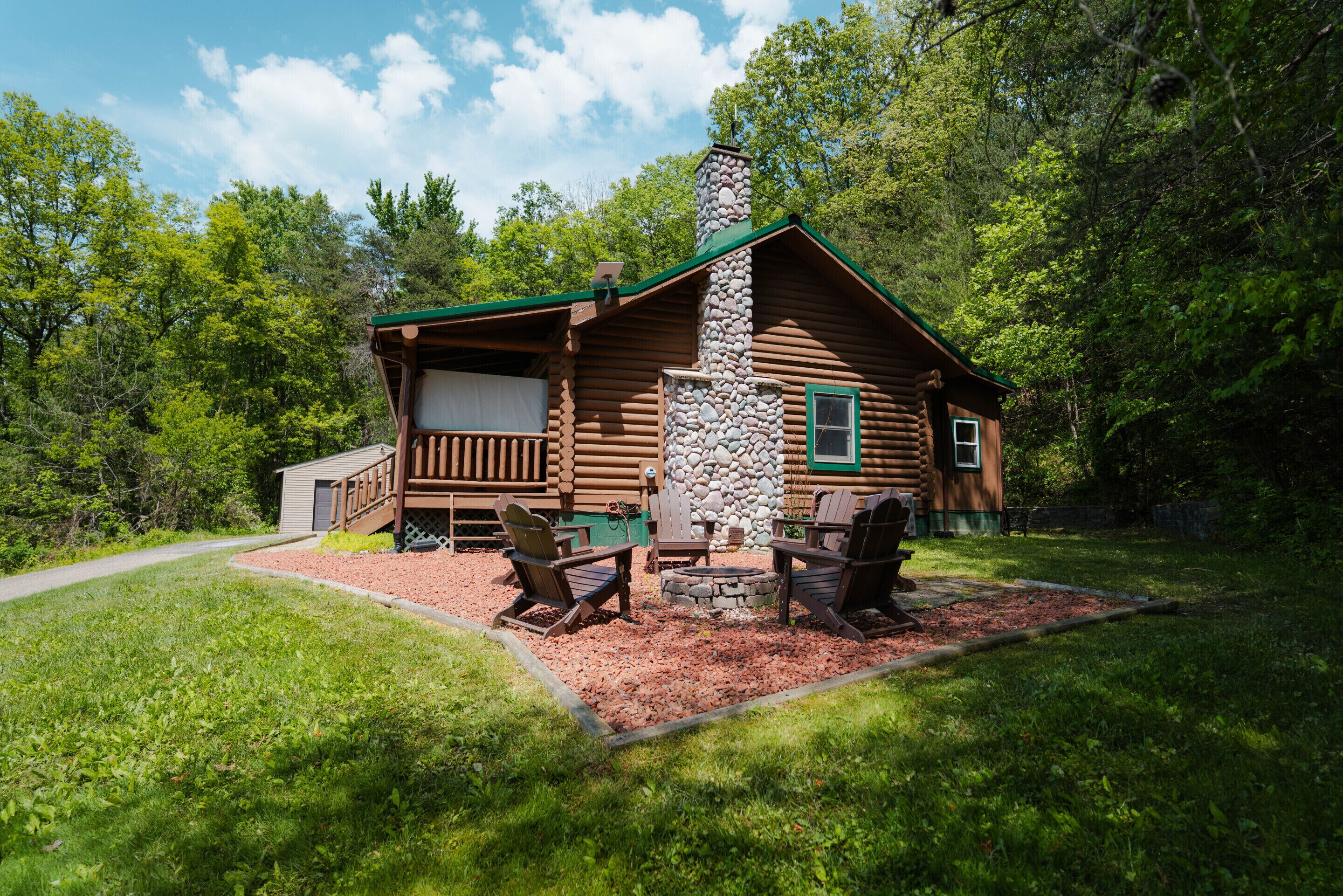 A log cabin with a stone chimney, a deck, and outdoor seating.