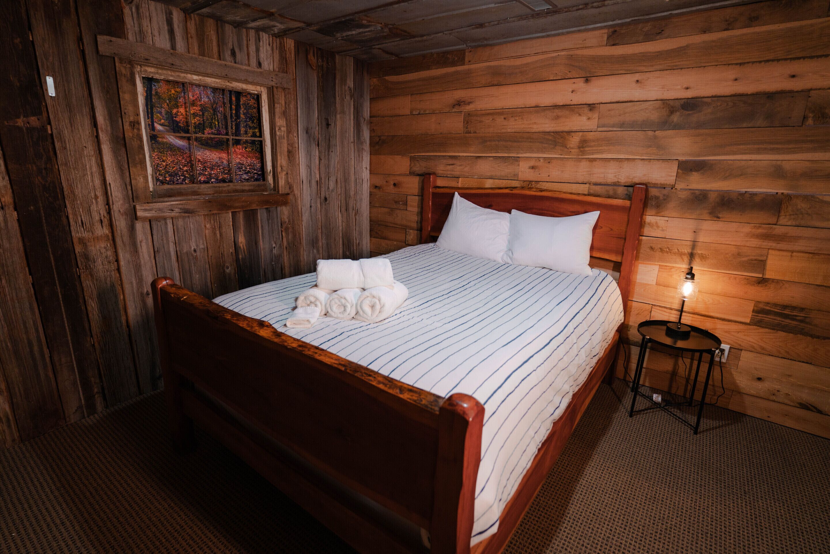 A wooden-paneled room with a bed, a small table, and a painting on the wall.