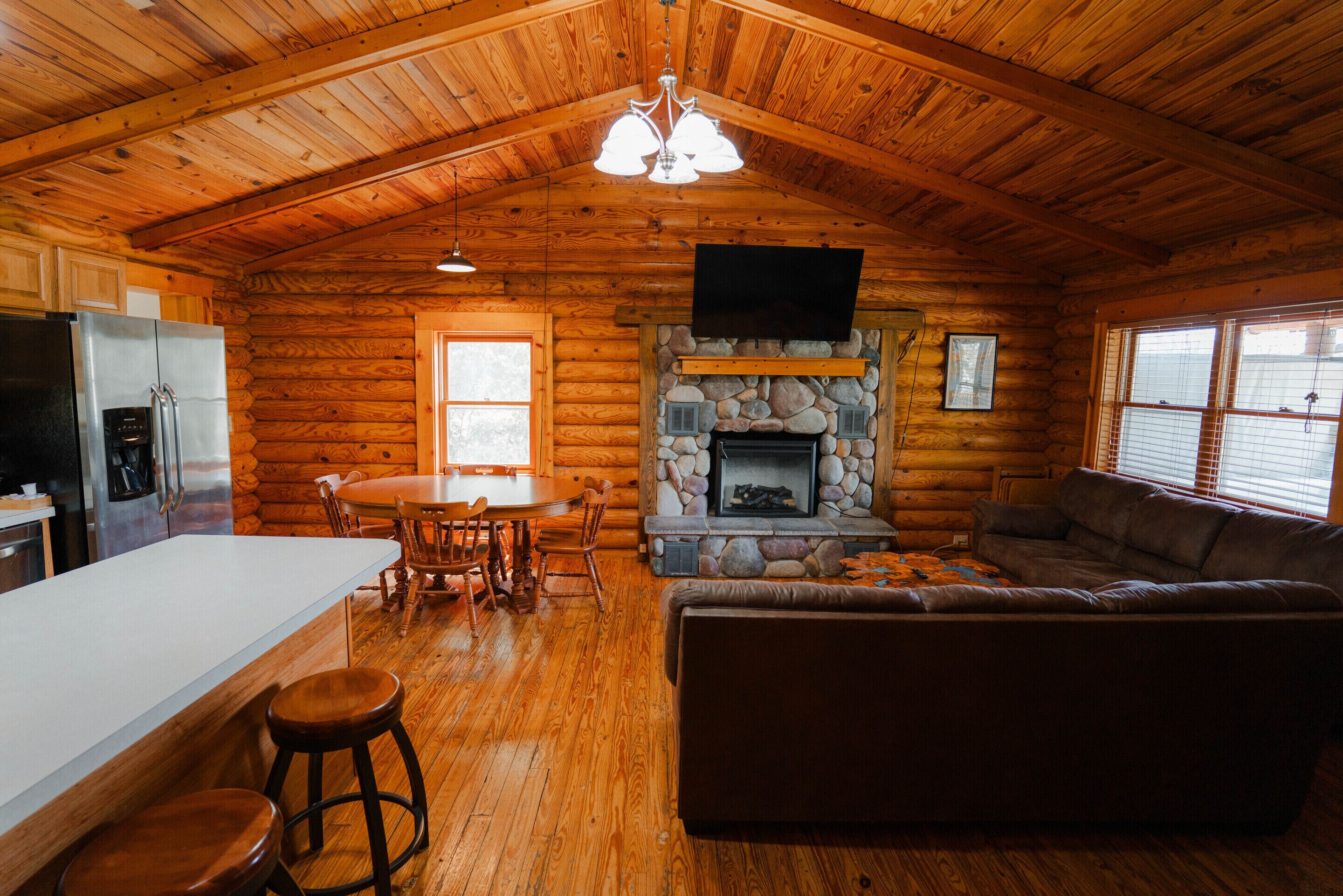 A log cabin interior with a kitchen, dining area, fireplace, and living room.