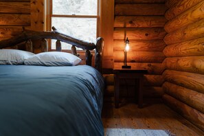 Ein Blockhaus-Zimmer mit einem Bett, einem Nachttisch und einem Fenster.