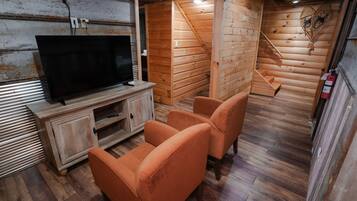 A wooden interior with a TV on a wooden cabinet, two orange chairs, and a wooden staircase.
