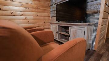 A wooden cabin interior with a television on a cabinet, wooden walls, and orange upholstered chairs.