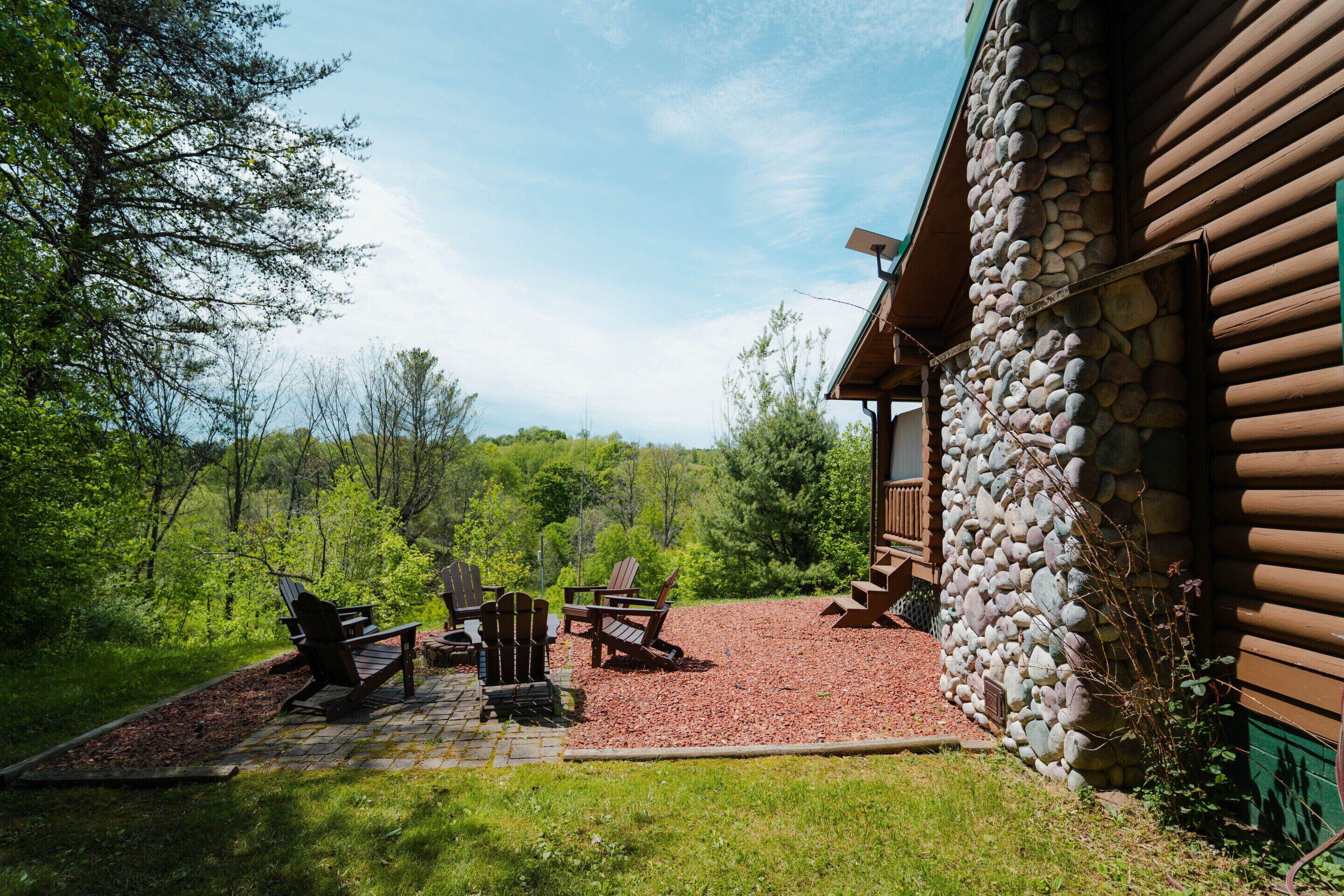 A log cabin with a stone exterior, a patio with Adirondack chairs, and a view of the surrounding forest.