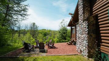 A log cabin with a stone exterior, a patio with Adirondack chairs, and a view of the surrounding forest.