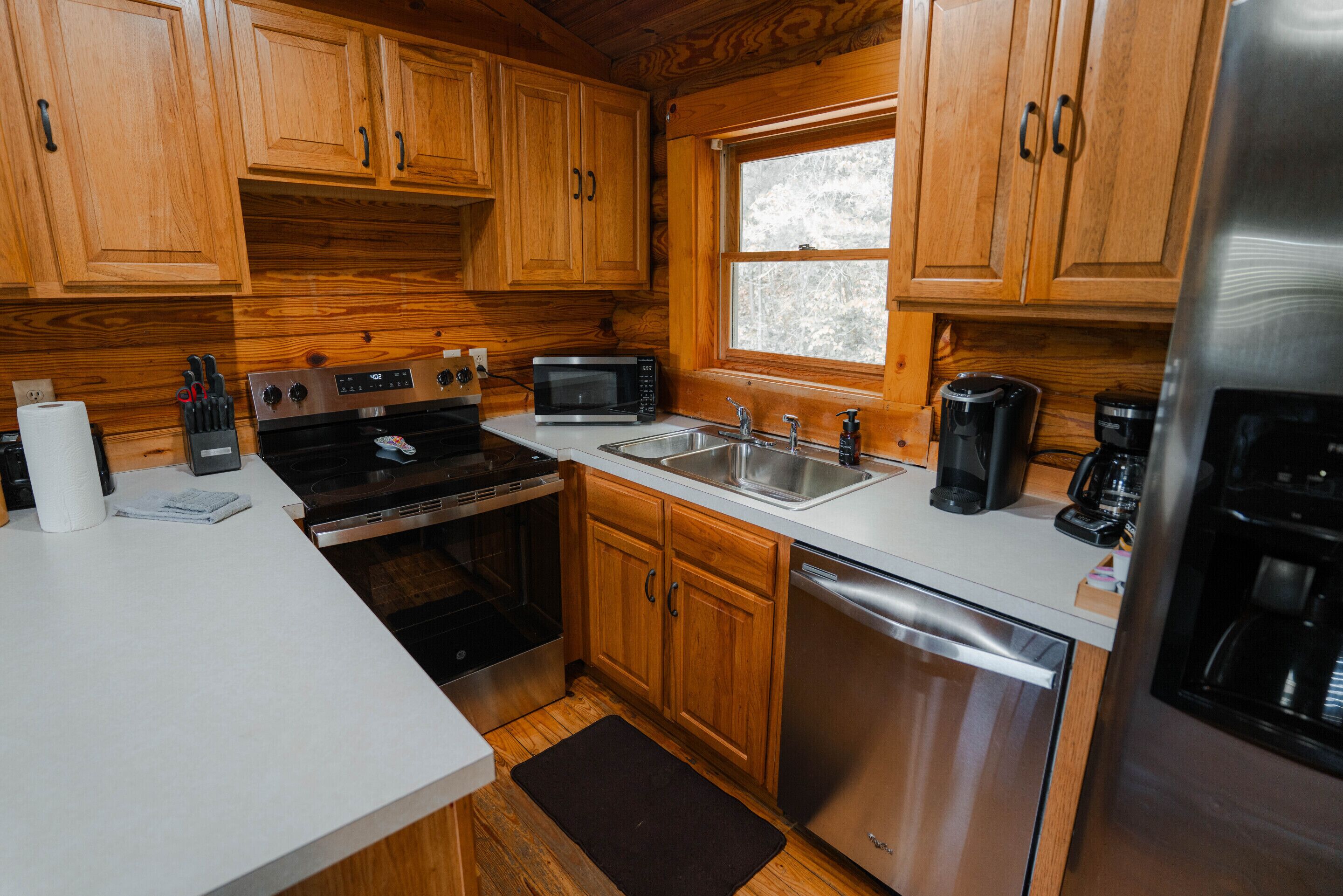 A kitchen with wooden cabinets, a stainless steel refrigerator, a microwave, a stove, a sink, and a dishwasher.