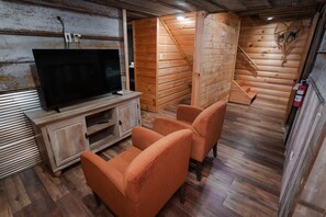 Ein Holzinnenraum mit einem Fernseher auf einer Holzkommode, zwei orangefarbenen Stühlen und einer Holztreppe.