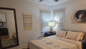 Un dormitorio con una cama grande, una mesita de noche con lámpara, un espejo y un tapiz decorativo en la pared.