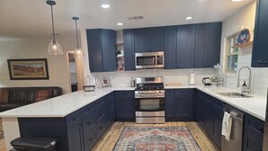 Una cocina moderna con armarios oscuros, una isla grande, electrodomésticos de acero inoxidable y una alfombra estampada.
