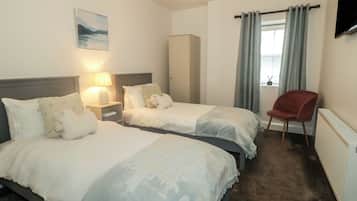 Habitación de hotel con dos camas, una silla roja, televisor, un cuadro y ventana con cortinas.
