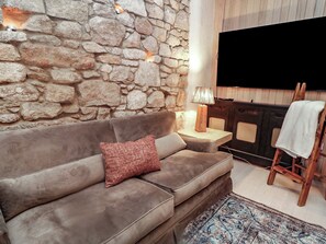 Un saló amb una paret de pedra, un sofà marró, una làmpada, un televisor i una taula petita.