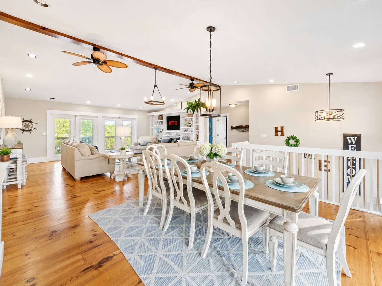 A spacious dining area with a wooden table and white chairs, a ceiling fan, and pendant lighting.