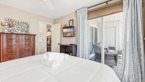 A hotel room with a bed, wooden dresser, TV, and a view of the outside. - Cherry Grove Condo Steps to Beach (North Myrtle Beach)