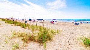 A beach with sand, grass, and a clear sky. - Cherry Grove Condo Steps to Beach (North Myrtle Beach)