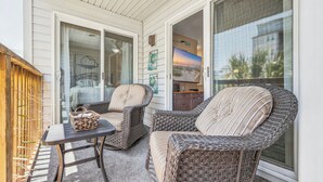 A covered patio with wicker furniture, a television, and a sliding glass door. - Cherry Grove Condo Steps to Beach (North Myrtle Beach)