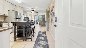 A modern kitchen with white cabinets, a black island, and a dining area with a patterned rug. - Cherry Grove Condo Steps to Beach (North Myrtle Beach)