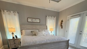 Quarto com uma cama grande, duas mesas de cabeceira, um ventilador de teto e uma janela com persianas.