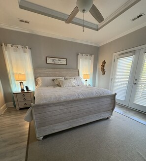 A bedroom with a large bed, two bedside tables, a ceiling fan, and a window with blinds. - The Lazy Turtle (Oak Island)
