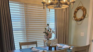 Uma sala de jantar com uma mesa de madeira, quatro cadeiras, um candelabro, um vaso com flores e uma grinalda na parede.