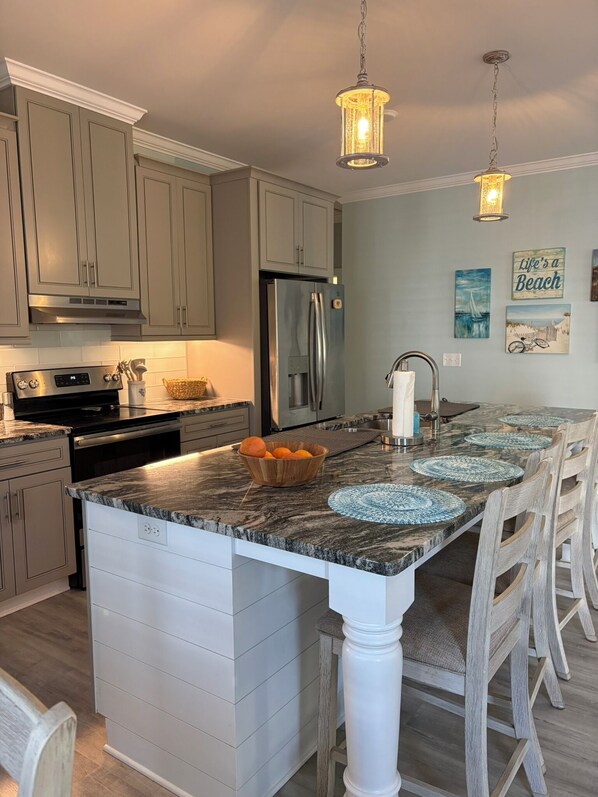 A kitchen with a central island, stainless steel appliances, and a hanging light fixture. - The Lazy Turtle (Oak Island)