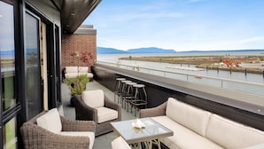 A balcony with wicker furniture, a glass table, and a view of a river and mountains. - Bellingham Waterfront Penthouse • Wraparound Balcony, Downtown & Near WWU (Bellingham)