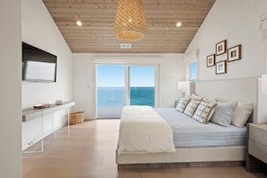 A bedroom with a bed, a bedside table, a TV mounted on the wall, and a large window with a view of the sea. - Luxury Oceanfront Retreat w/ Hot Tub, Fire Table & Pacific Views near S.F. (Moss Beach)