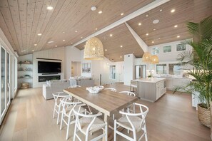 A spacious kitchen with a wooden ceiling, a dining area with white chairs, and a large island. - Luxury Oceanfront Retreat w/ Hot Tub, Fire Table & Pacific Views near S.F. (Moss Beach)