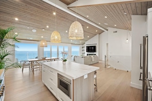 Cozinha moderna com uma ilha grande, luminárias pendentes e vista para o oceano.
